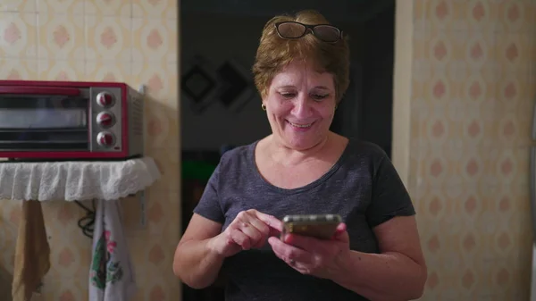 Старшая Женщина Которая Пользуется Телефоном Стоя Дома Кухне Переписываясь Телефону — стоковое фото