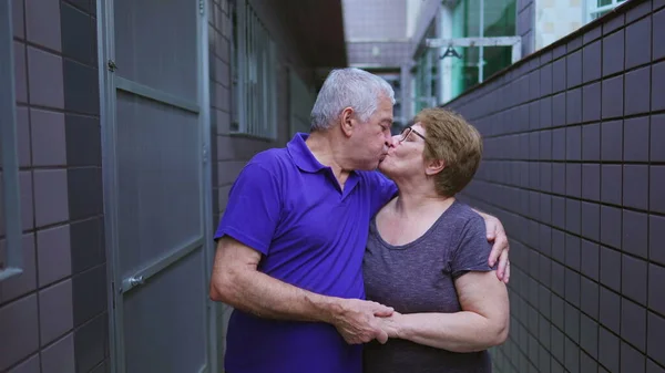 Senior couple kissing in loving embrace standing in backyard residence. South American elderly married husband and wife