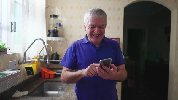 Радісний Старший Чоловік Тримає Мобільний Пристрій Стоїть Біля Кухонної Раковини — стокове фото