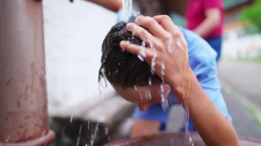 Genç çocuk sıcak yaz gününde Avrupa 'da halka açık Fountain caddesinde saç ve saç yıkıyor. Genç bir çocuk kendini tazeliyor. Suyun yavaş çekimde aktığını hissediyor.