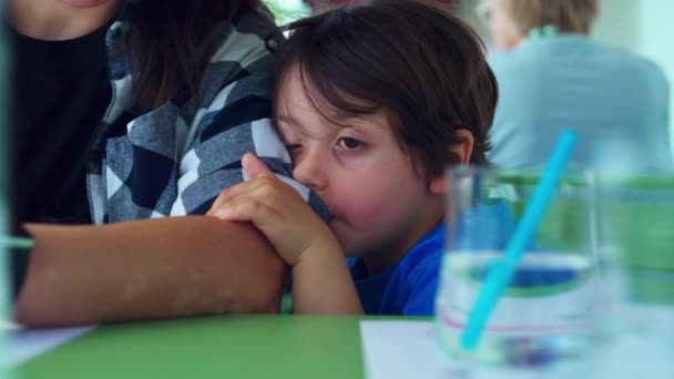 疲惫的小男孩靠在妈妈的胳膊上 在餐馆等着食物的到来 感到厌烦 小孩依偎在妈妈的脸上 鬼鬼祟祟的 — 图库视频影像