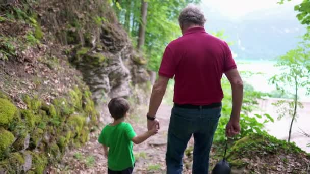 祖父は トレイルパスを歩いている孫と手を握り 家族は屋外でハイキング 世代間ボンディングシーン おじいちゃんと子供と一緒に — ストック動画