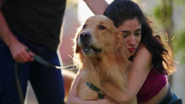 Parkta Golden Retriever köpeğini kucaklayan bir kadın. Hafta sonu eğlenen bir çift. İnsanlar gün ışığında evcil hayvanlara sarılır.