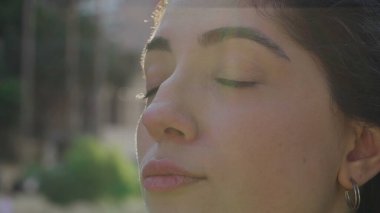 Meditasyon yapan genç bir kadın, doğadaki farkındalıkla gözlerini kapatıyor. 30 'lu yaşlarda düşünceli bir kadın. Yüzü açık, gülümseyen, rahatlamış.