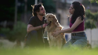 Samimi çift, güneş ışığında Golden Retriever evcil hayvanıyla parkta yaz gününün tadını çıkarıyorlar.