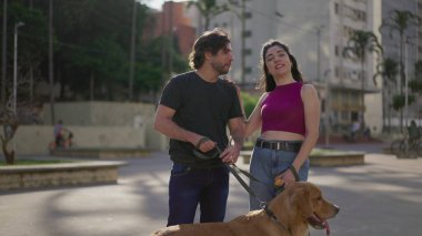 Mutlu çift dışarıda köpekleriyle kameraya poz veriyor. Kadın ve erkek tasmalı Golden Retriever Pet ile ayakta duruyor. Rahatlamış insanlar hafta sonu aktivitelerinin tadını çıkarıyor