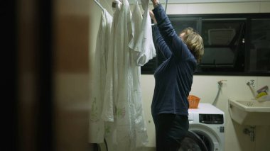 Çamaşır askısında kurutmak için çamaşırlarını koyan yaşlı bir kadın. Ev işlerini yapan yaşlı bir adamın gerçek hayat sahnesi.