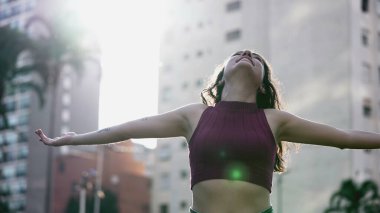 Neşeli kadın kollarını açıp güneşin sıcağında güneşleniyor, doğanın güzelliğini takdir ediyor ve hayata şükrediyor.