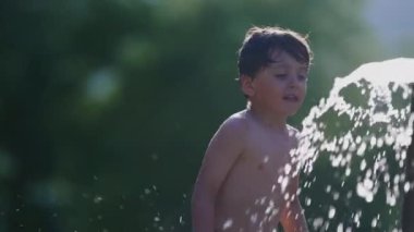 Belediye havuzunda havuz başında havuz başında güneşlenen küçük bir çocuk. Yüzme yerindeki fıskiyelerden gelen şen şakrak sulardan zevk alan çocuk.