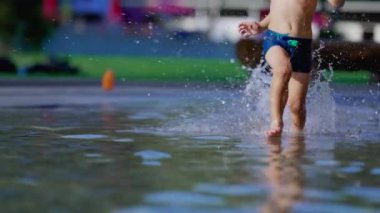 Neşeli çocuk yaz günü havuzda ağır çekimde koşuyor. 120fps 'de koşan ve su sıçratan aktif küçük bir çocuk.
