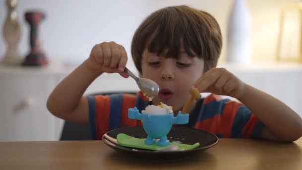 小さな男の子が柔らかい沸騰した卵を食べて コックを食べる 子供はスプーンで自分自身で軽食を食べる — ストック動画