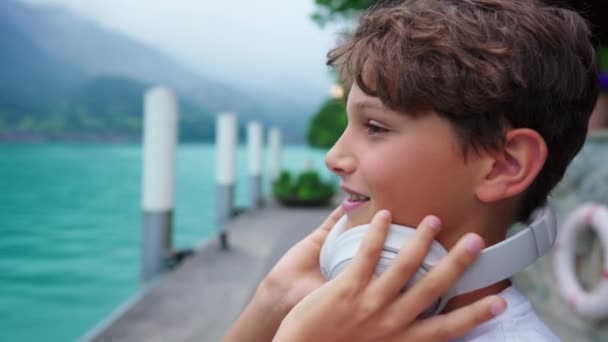 ハンサムなティーンボーイ 音楽と考え的な湖畔のビュー 自然を鑑賞するためにヘッドフォンを離れて子供のプロフィールのクローズアップ顔 — ストック動画
