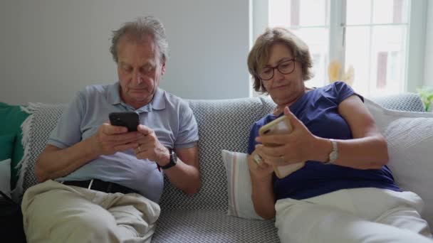 Старшая Супружеская Пара Смотрит Свои Мобильники Сидя Диване Пожилые Мужчины — стоковое видео