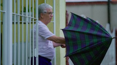 Olgun bir adam kötü havada şemsiye açar. Yaşlı beyaz adam yağmur yağarken evden çıkıp sokağa çıktı.