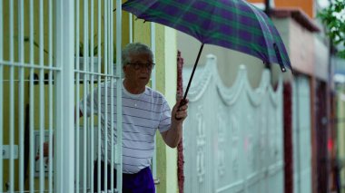 Yaşlı adam yağmur yağarken evden çıkıyor, şemsiyeyi açıyor ve arkasından kapıyı kapatıyor. Yaşlı adam kaldırımda yürüyor.