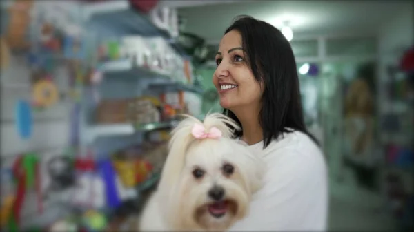 店でペット製品をブラウズしながら小さな犬を抱えている女性 — ストック写真