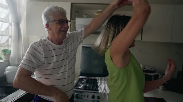 Happy romantic older couple dancing together in kitchen, retired senior enjoying the golden years in joyful embrace and dance