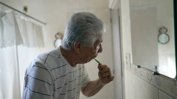 古い朝のルーチンでカジュアルな国内シーンでトイレミラーの前に歯を磨くシニアマン 高齢者 成熟した — ストック写真