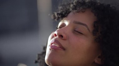 Meditasyonda gözlerini kapatan düşünceli genç bir siyah kadın. Ruhani Afrikalı Amerikalı yetişkin kız gülümseyerek gökyüzüne bakıyor.