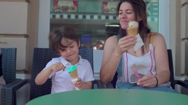 パーラーショップの外でアイスクリームコーンを楽しむハッピーマザーと子供 ママと息子は 甘いデザートトリートを食べて味わう 笑顔の表情 — ストック動画