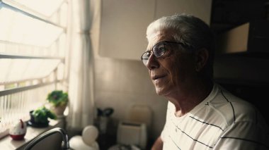 Düşünceli yaşlı bir adam mutfaktan dışarı bakıyor. Hayatı yansıtan olgun bir erkeğin düşünceli meditasyoncu bakışları.