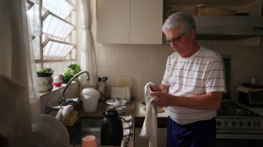 Mutfak lavabosunda mutfak malzemelerini kurutan emekli kıdemli bir adam. Ev işleri yapan yaşlı bir insanın ev hayatı.