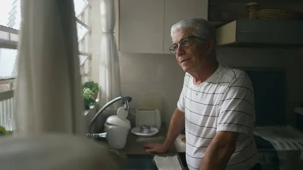Homem Sênior Atencioso Olhando Para Fora Janela Cozinha Apoiando Contador — Fotografia de Stock
