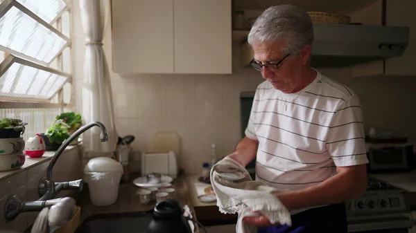 台所の流しに立つ台所用品を乾燥させる退職者の上級者 ホームルーチンを行う高齢者の家庭生活シーン — ストック写真