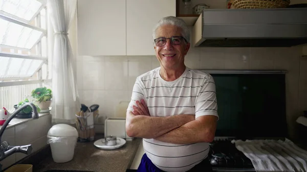 一位快乐的老人站在自家厨房的窗前 双手叉腰对着相机微笑 — 图库照片