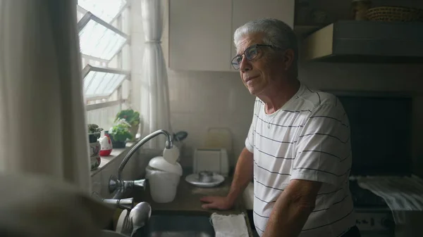有思想的老人凝视着厨房的窗户 靠在柜台上 退休老人凝视着窗外思考 — 图库照片