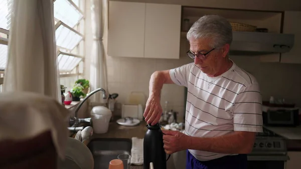 一个成熟的男人在厨房的水槽边把装有热水瓶的咖啡倒入杯子里 退休老人的真实家庭生活场景从每日上午开始 — 图库照片