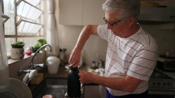 一个成熟的男人在厨房的水槽边把装有热水瓶的咖啡倒入杯子里 退休老人的真实家庭生活场景从每日上午开始 — 图库照片