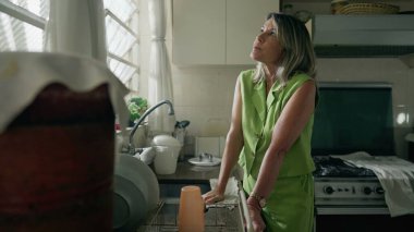 Endişeli orta yaşlı bir kadın mutfakta duruyor ve stres ve sıkıntıdan muzdarip. 50 'li yaşlarda beyaz bir kadın pişmanlık ve endişe duyuyor.