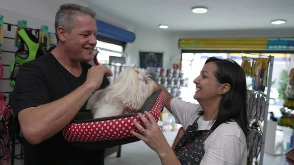 Happy Pet client holding his Small Dog after bath. Female business owner of Pet Store handing Shih-Tzu to man after grooming bath