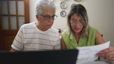 Evde dizüstü bilgisayarın önünde finansal sorunları tartışan sıkıntılı yaşlı çift. Üzüntülü karı koca araba konusunda tartışıyor.