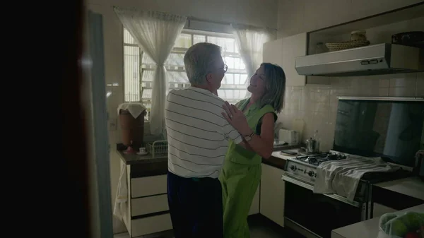 Romantic senior couple dancing in kitchen setting, retired older man and woman engaged in dance at home, authentic domestic lifestyle scene