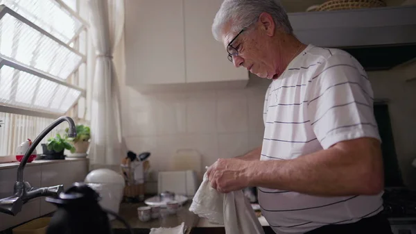 退休老人站在窗边厨房用毛巾擦干茶杯 从事家庭生活活动的老年人 — 图库照片
