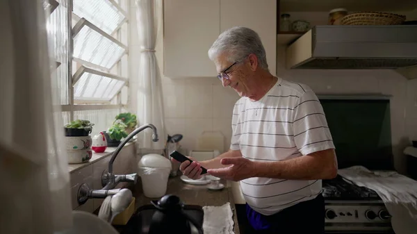 老年人站在厨房时对手机的好消息反应很高兴 — 图库照片