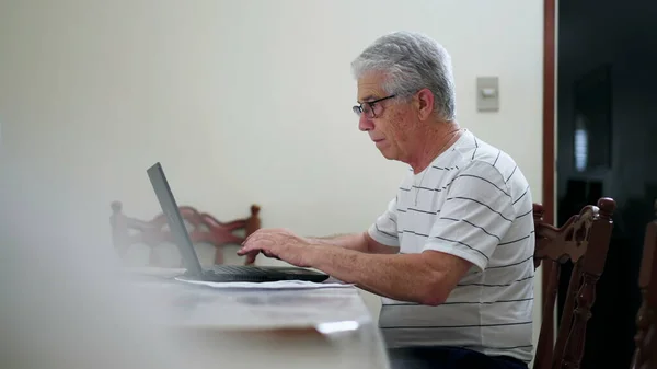 他在家里用笔记本电脑键盘打字 一个从事现代技术的老年人凝视着电脑屏幕的真实的家庭场景 — 图库照片
