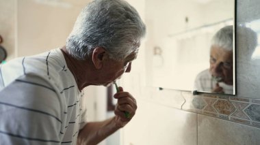 Son sınıf sabah rutini aynada fırçalarken banyo aynasında kendi yansımasına bakıyor. Diş hijyeni, güne başlayan yaşlı insan.