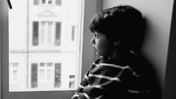 窓のそばに座っている一人の年寄りの思慮深い子供は 建物の住居から通りに向かい モノクロマティックな黒と白の思慮深い子供の視線 — ストック動画