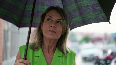 Şehir caddesinde şemsiye tutarken yağmurda yürüyen neşeli kadın.