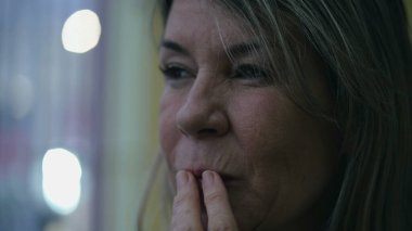 Düşünceli, orta yaşlı bir kadın akşamları sokağa bakıyor. Düşünceli, olgun bir insanın yakın plan yüzü.