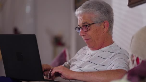 全神贯注的老人坐在家里的沙发上 用笔记本电脑打字 年龄较大的男性高加索人 从事现代技术 撰写电子邮件 — 图库视频影像