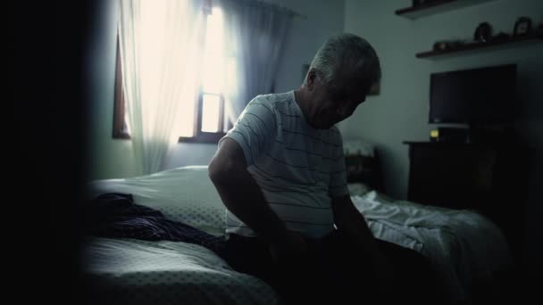 ソンバーベッドルームのベッドサイドに座っているうつ病の年配の男性 一人で苦しんでいる孤独な高齢者の劇的な暗くて暗いシーン — ストック動画
