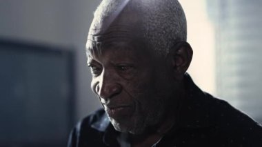 Derin düşüncelere dalmış yaşlı siyah bir adam sessizce odada oturup düşünüyor. Düşünceli Afro-Amerikalı insan yüzünü odaya yakın plan yapıyor.