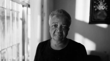 Üst düzey siyahi bir kadının dramatik portresi. Pencerenin yanında dikilip tek renkli kameraya bakıyor. Yaşlı Brezilyalı bir kadının bilgelik konsepti