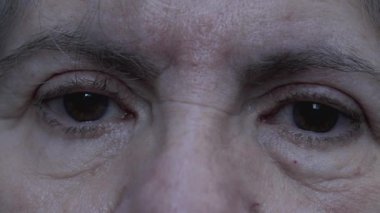 Yaşlı, hasta bakışlı yaşlı bir kadının dramatik makro çekimi. Yaşlı bir insanın kameraya bakmaktan yorgun düşmesi.