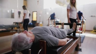 Yaşlı Kadın Pilates Makinesinde Kadın Koçun rehberliğinde Geriniyor, Stüdyo oturumu sırasında Yaşlılar Egzersiz Yapıyor