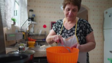 Evde yemek pişirmeye odaklanmış yaşlı bir kadın, önlük giymiş büyük anne öğle yemeği hazırlıyor.